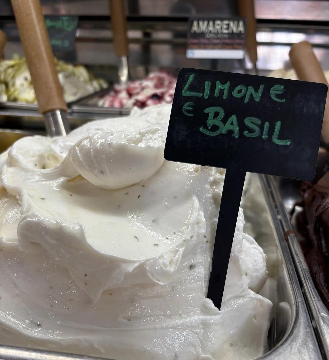 Tina de gelado branco com uma etiqueta preta onde se lê Limone e Basil, numa vitrine de gelados